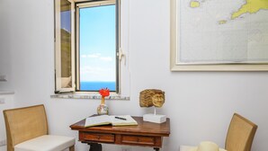 Quarto com escrivaninha, duas cadeiras, janela com vista, vaso e mapa na parede.