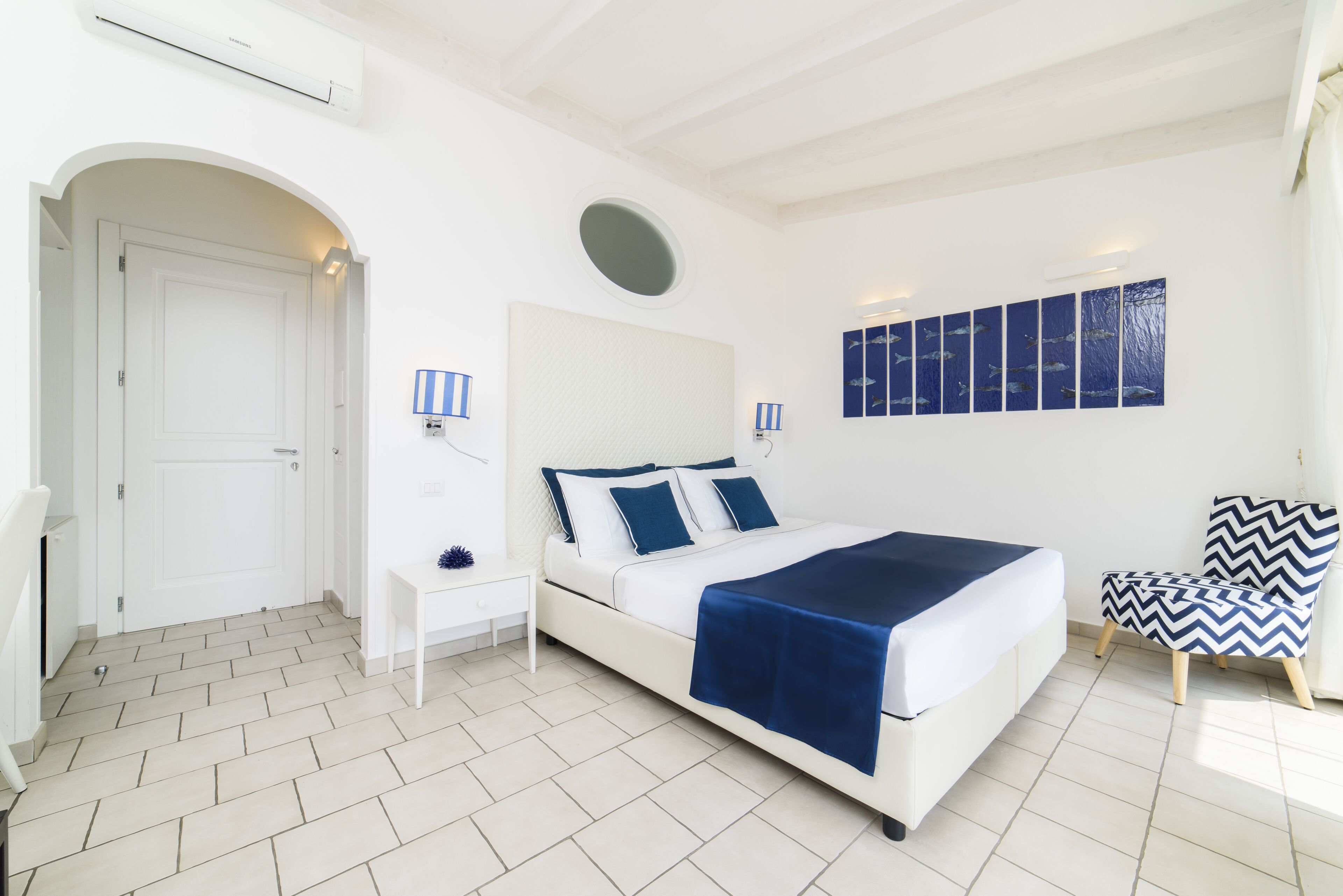 Ein Schlafzimmer mit Bett, Nachttisch, Stuhl und einem Wandbild.