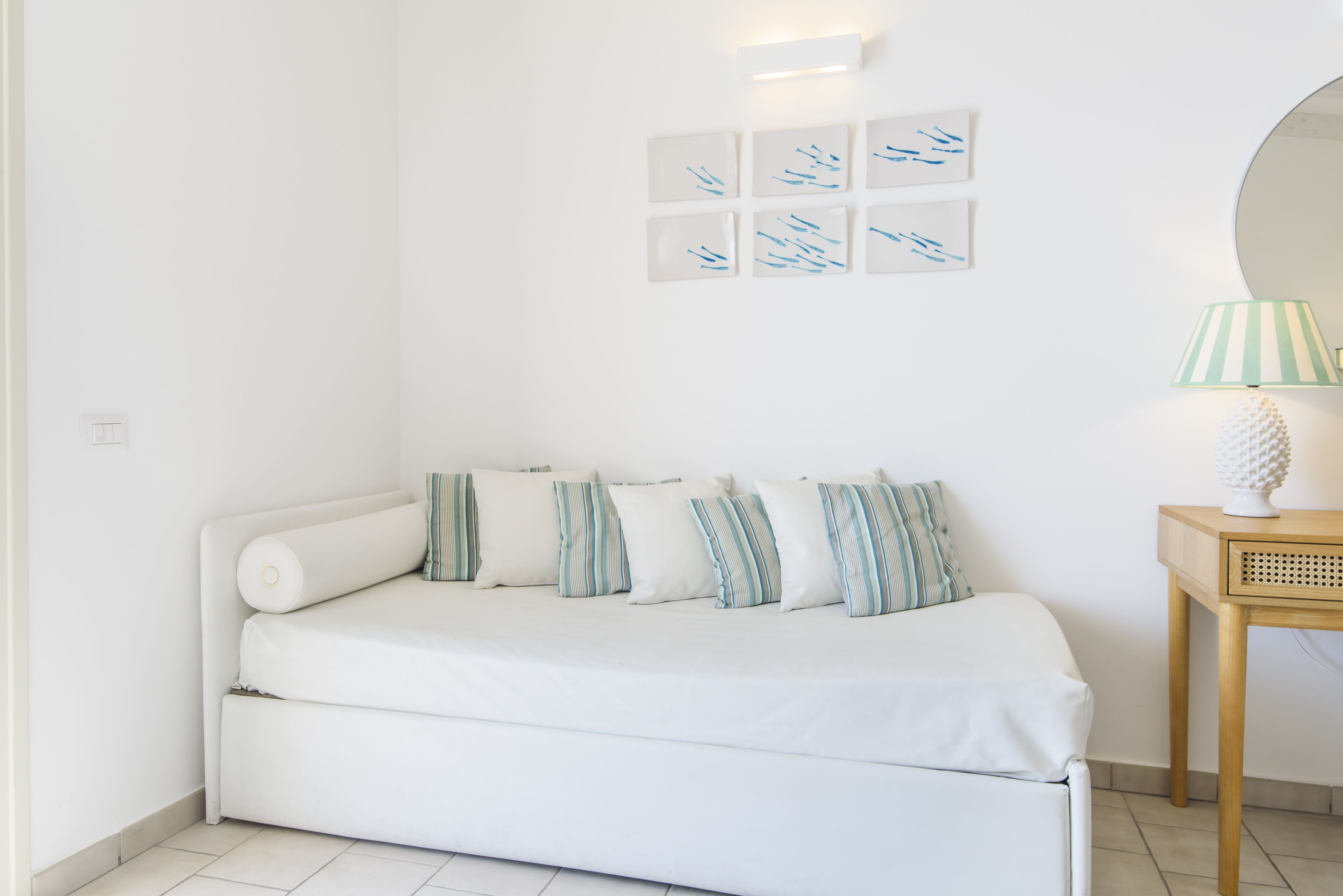 A white sofa with striped pillows, a small table with a lamp, and wall art.
