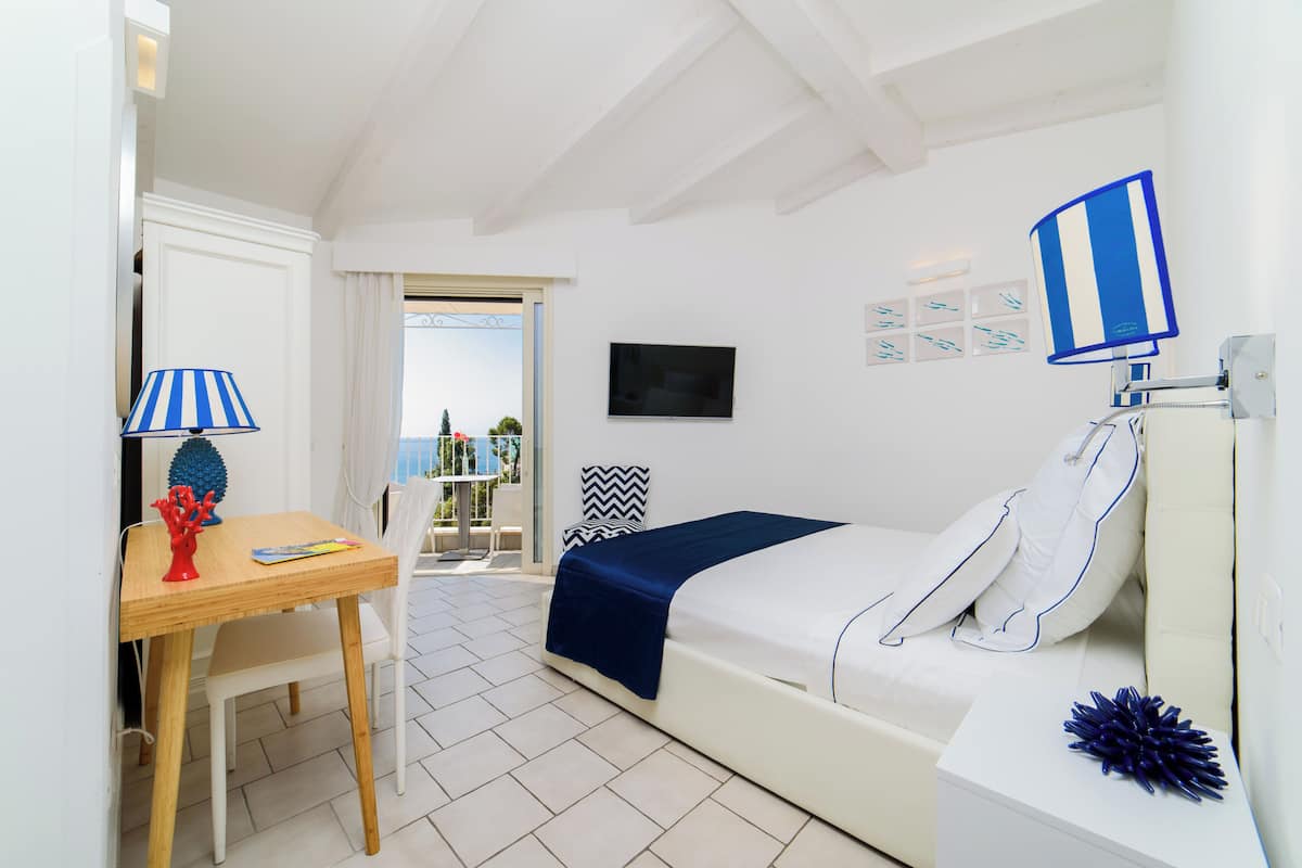 Une chambre d’hôtel avec un lit, un bureau, une chaise, une télévision et un balcon avec vue.