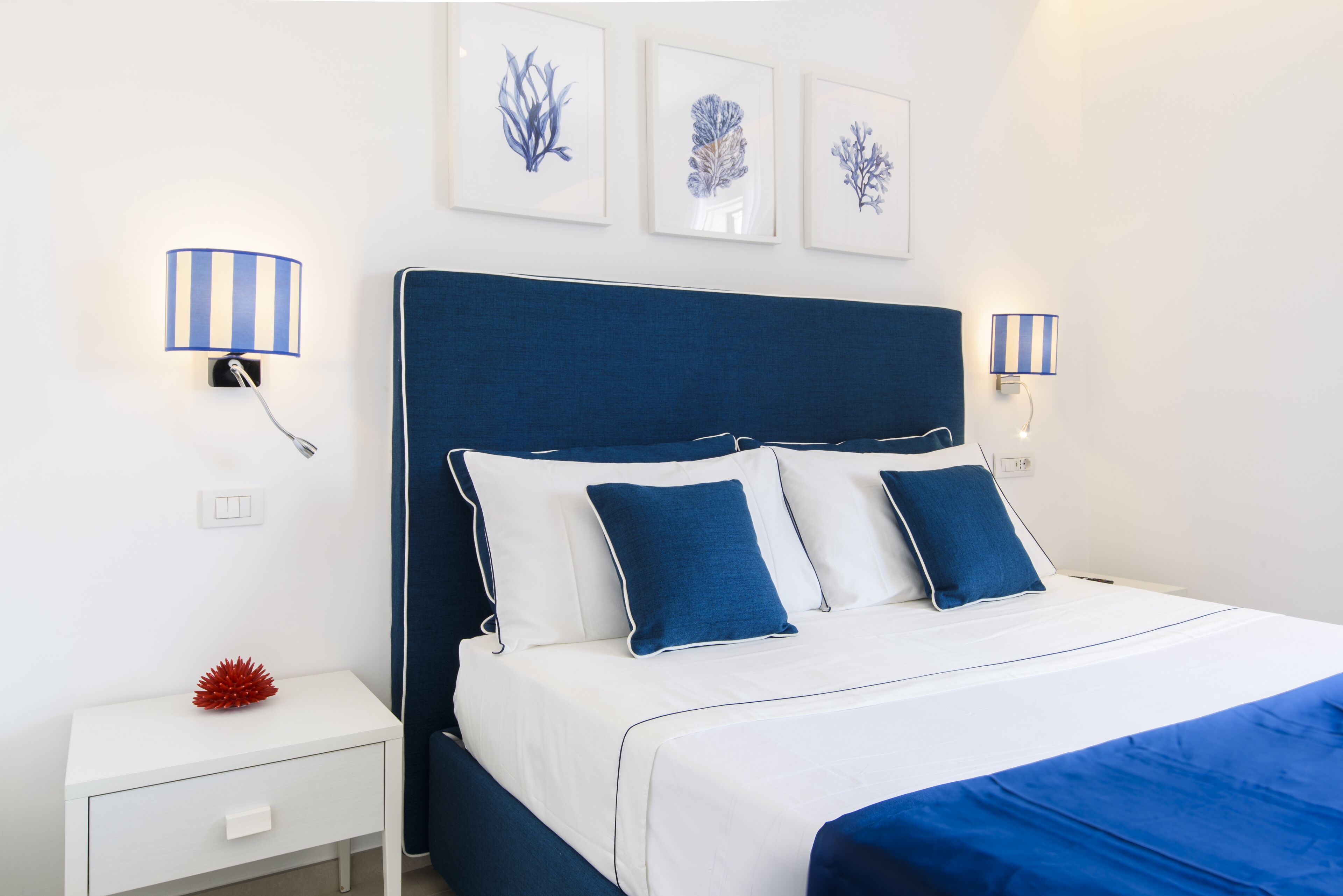 A neatly arranged bedroom with a bed, bedside lamps, a nightstand, and wall art.