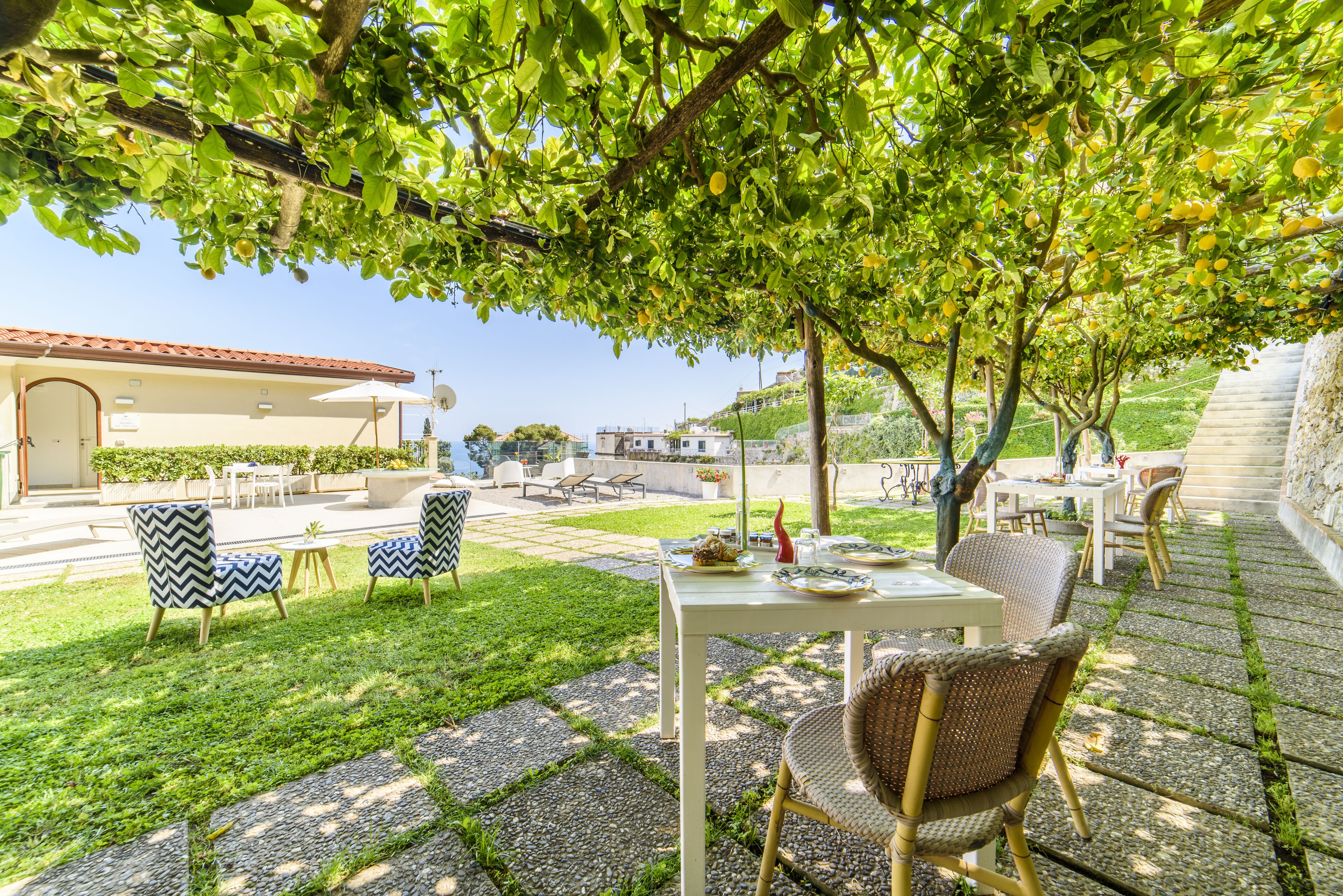 An outdoor patio area with a table and chairs, surrounded by greenery and a stone pathway.
