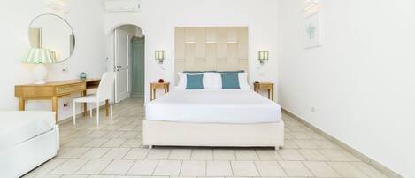 A modern bedroom with a large bed, a desk, and a chair. There are two bedside tables with lamps.