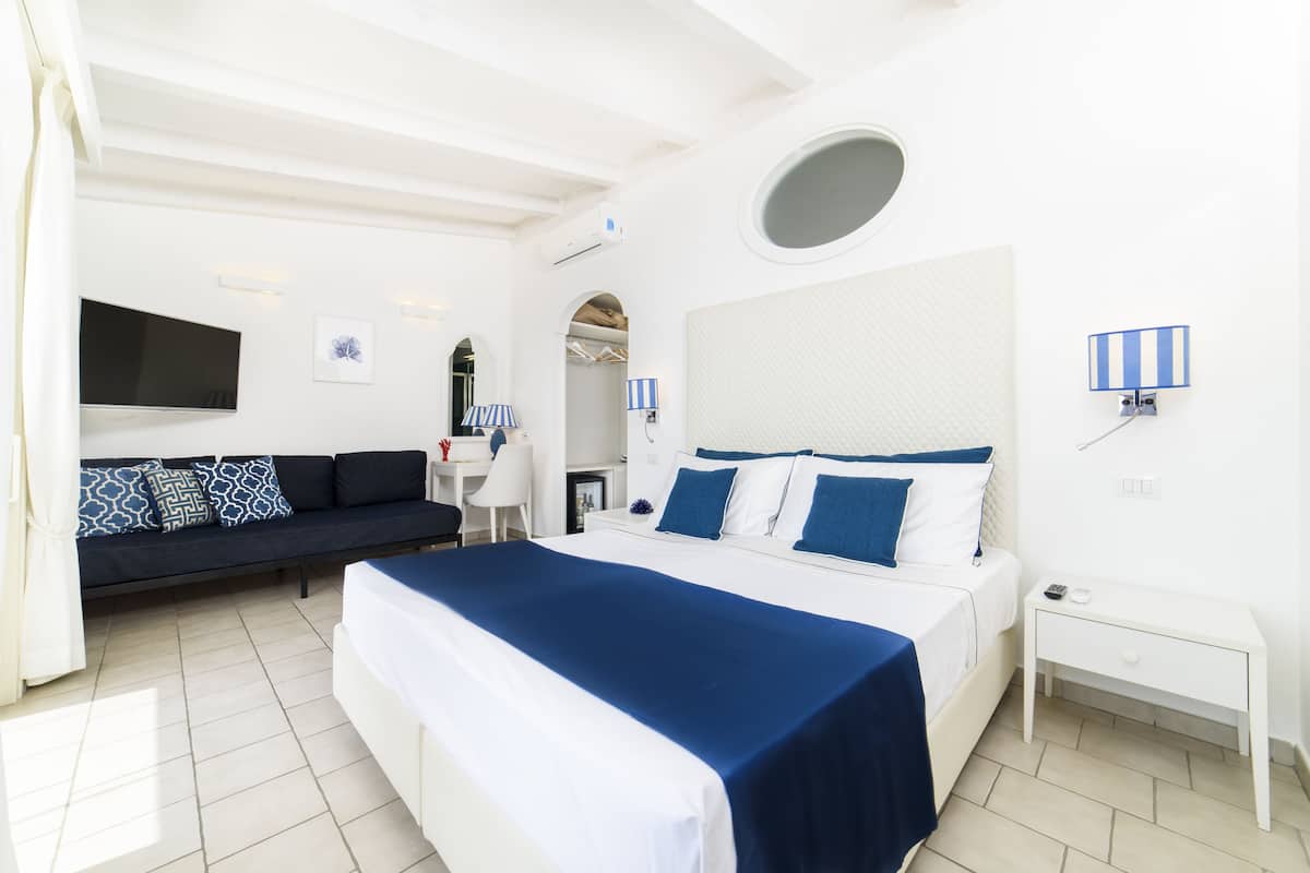 Une chambre d’hôtel moderne avec un grand lit, un canapé, une télévision et un petit bureau.