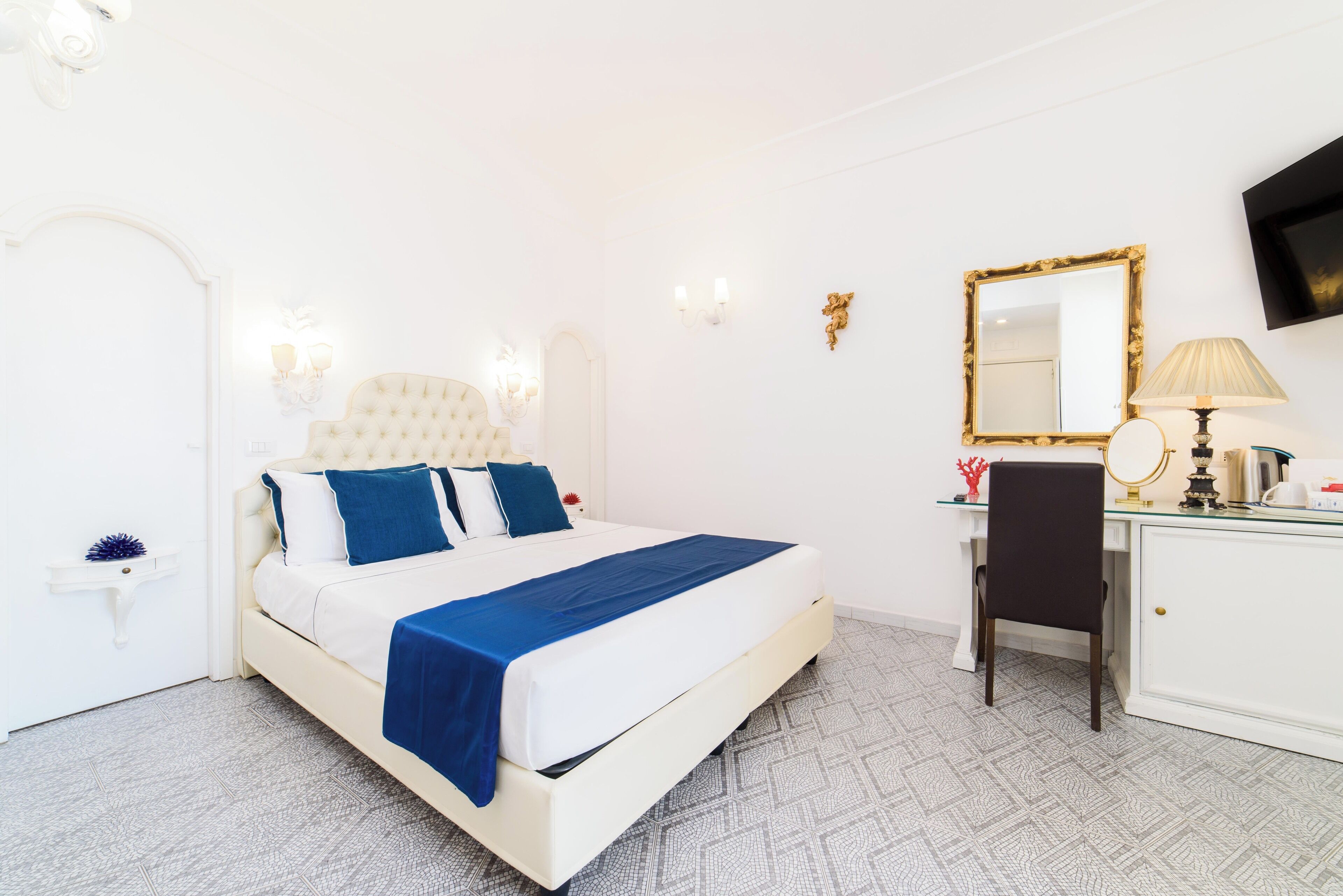 A hotel room with a bed, a desk, a chair, a mirror, and a television on the wall.