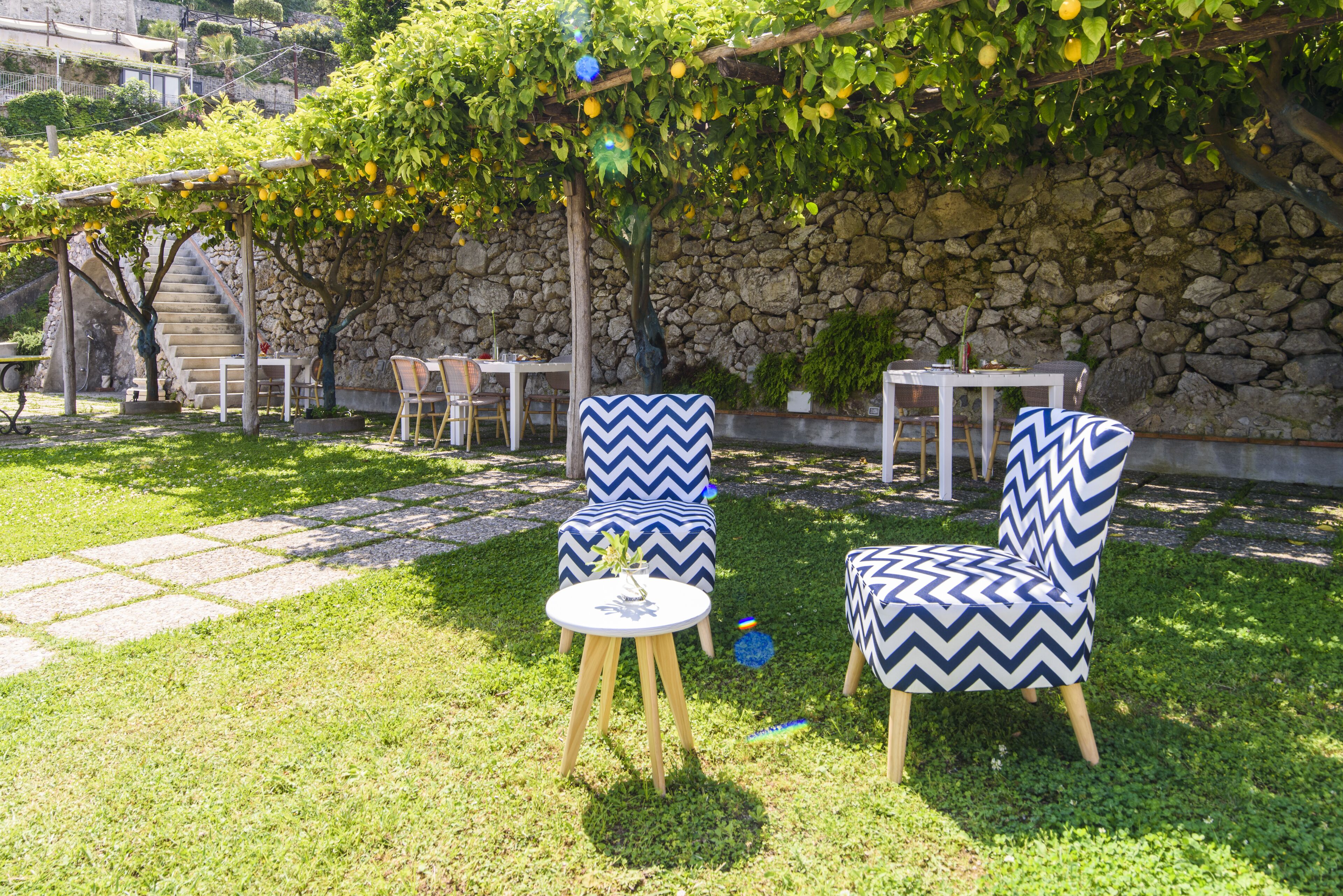 Eine Terrasse mit zwei Stühlen und einem kleinen Tisch, umgeben von einer Steinmauer und einer Rasenfläche.