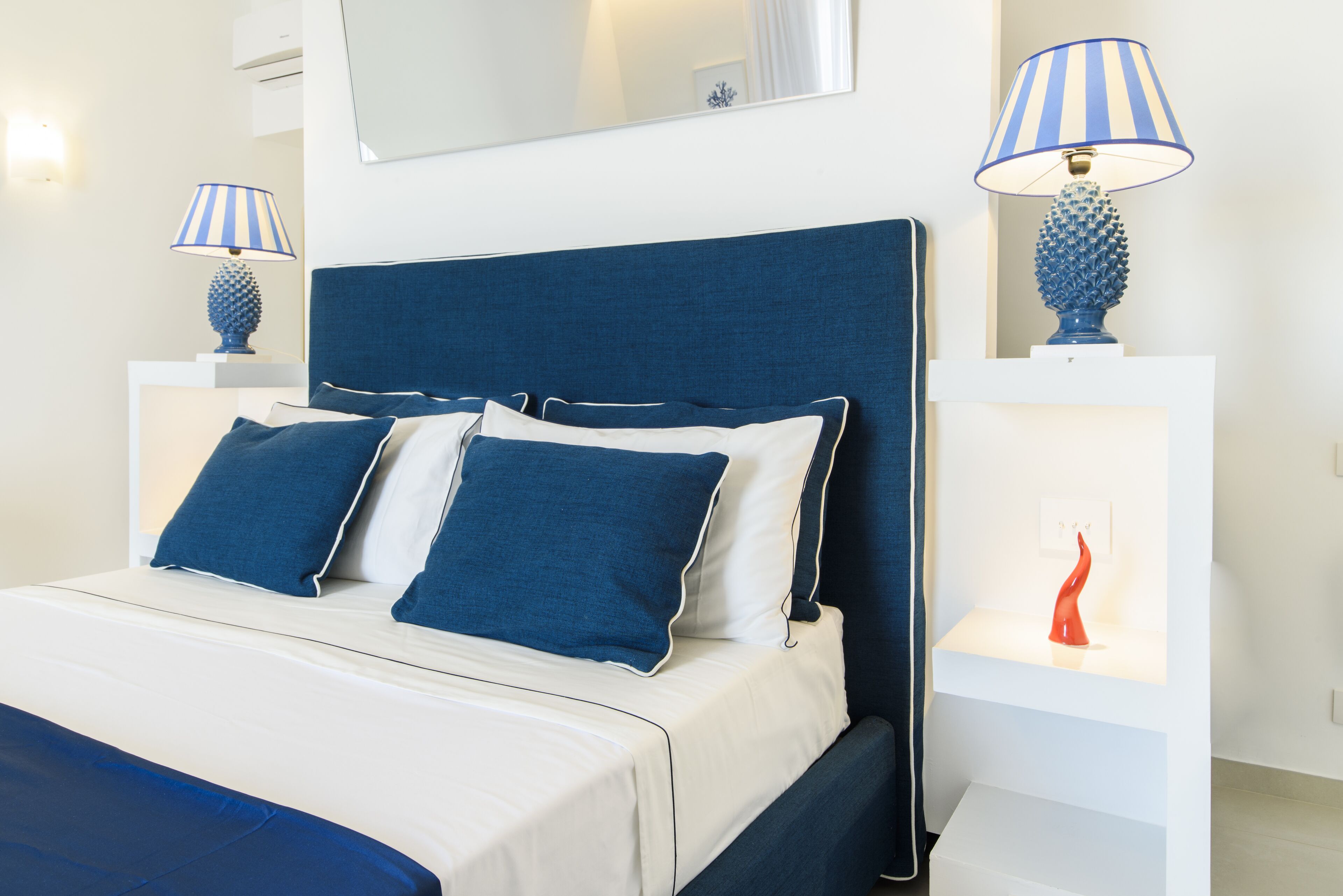Ein ordentlich bezogenes Bett mit blau-weißer Bettwäsche, einem blauen Kopfteil und zwei Nachttischen mit Lampen.