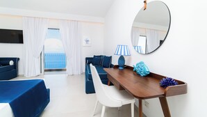 Quarto de hotel com cama, escrivaninha, cadeira, televisão, janela com cortinas e vista para o mar.