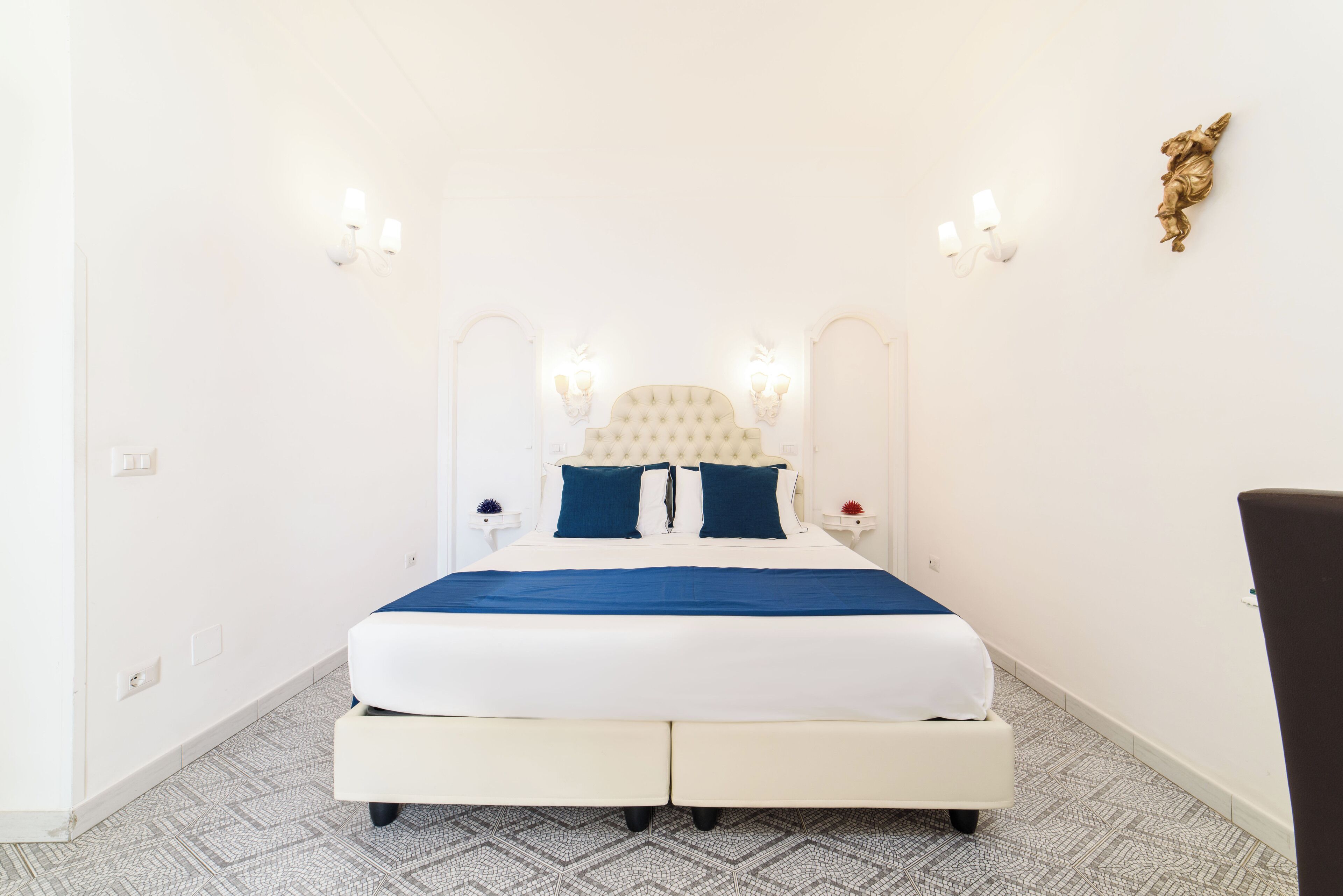 A neatly made bed with a white headboard and blue bedding, two bedside tables with lamps, and a patterned floor.