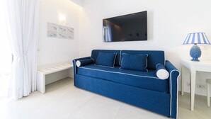 Uma sala moderna com um sofá azul, uma televisão de tela plana, um banco branco e uma luminária.