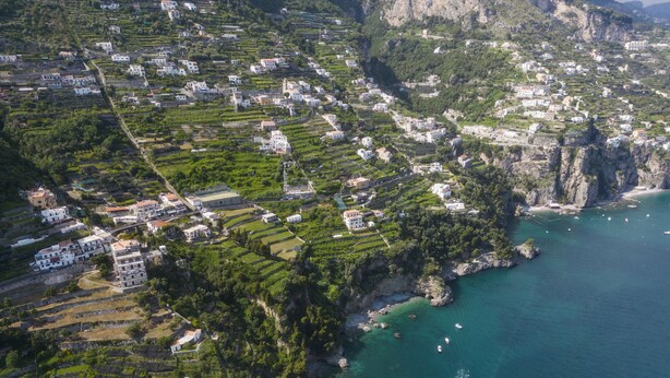 An aerial view of a coastal town with terraced houses, a clear blue sea, and a boat creating a wake. - Residenza Al Pesce d'Oro (Amalfi)