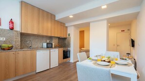 A modern kitchen with wooden cabinets, a microwave, and a dishwasher. There is a dining area with a table set for two, and a fire extinguisher mounted on the wall.