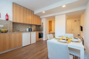 A modern kitchen with wooden cabinets, a microwave, and a dishwasher. There is a dining area with a table set for two, and a fire extinguisher mounted on the wall.