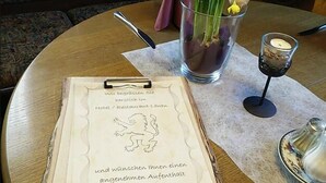 A table with a menu, a vase with yellow flowers, and a candle holder. - Hostel zum Löwen (Todtmoos)