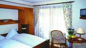 A hotel room with a wooden bed, a small table with a lamp, and a chair. - Hostel zum Löwen (Todtmoos)