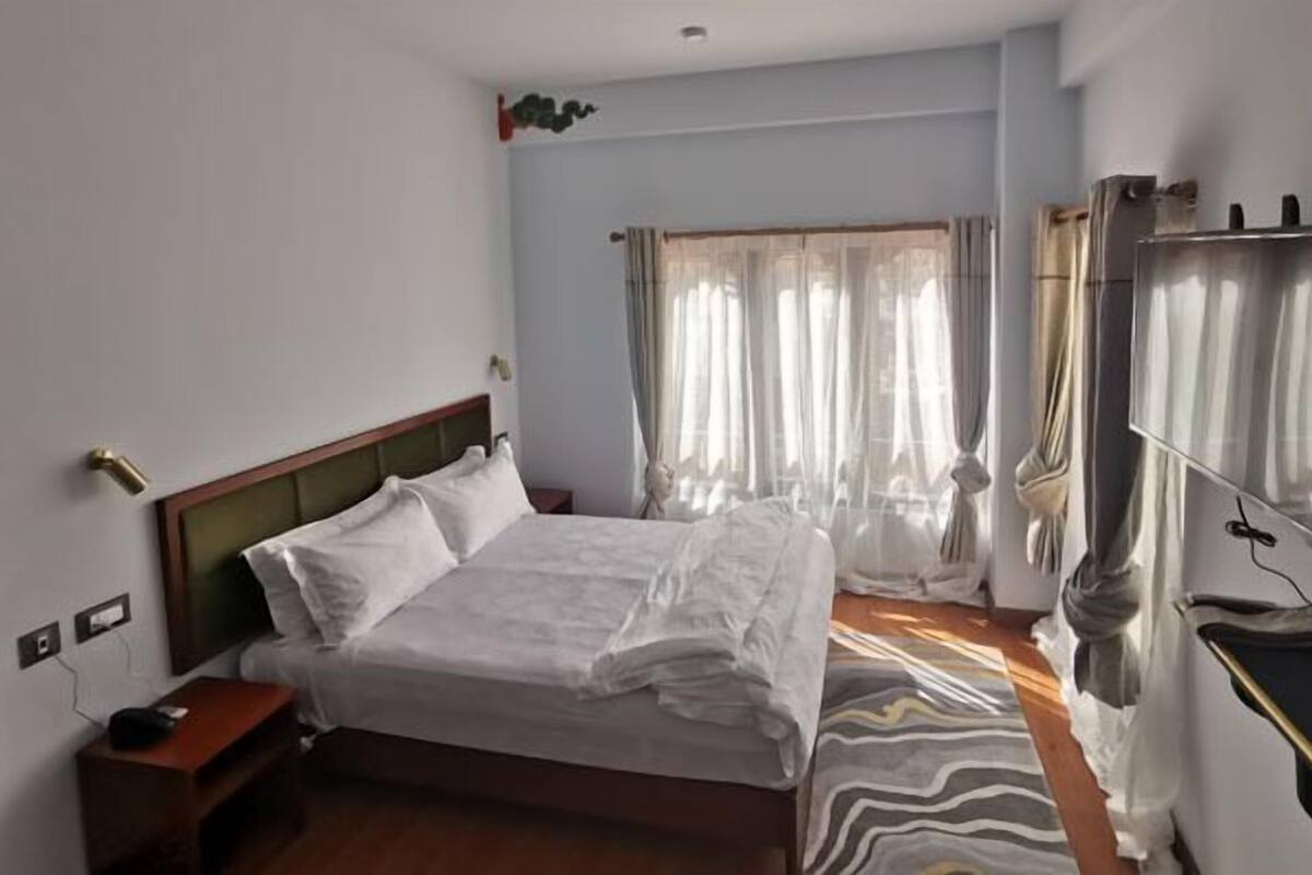 A hotel room with a bed, bedside table, and a TV mounted on the wall.