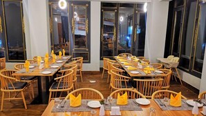 Un restaurante con varias mesas dispuestas, servilletas amarillas, sillas de madera y una decoración de estilo moderno.