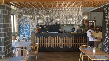 Interior de restaurante con mesas de madera, una barra y adornos metálicos colgantes.