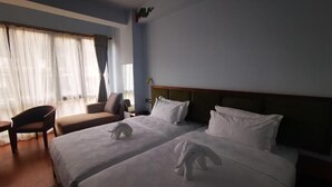 Habitación de hotel con dos camas, una silla, un escritorio y un ventanal con cortinas.