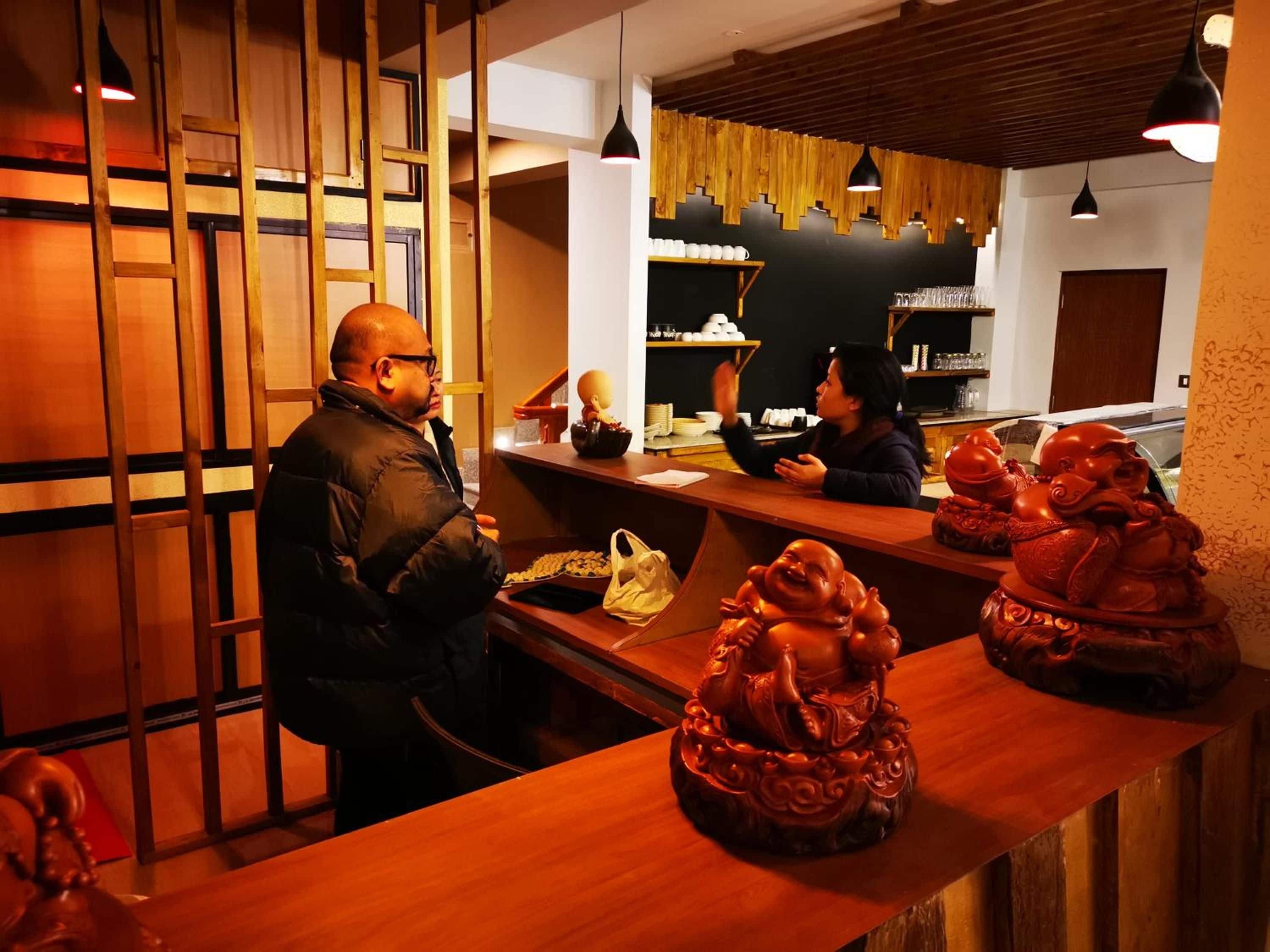 Interior de un restaurante con decoración de madera, una barra con una caja registradora y una persona sentada en la barra.