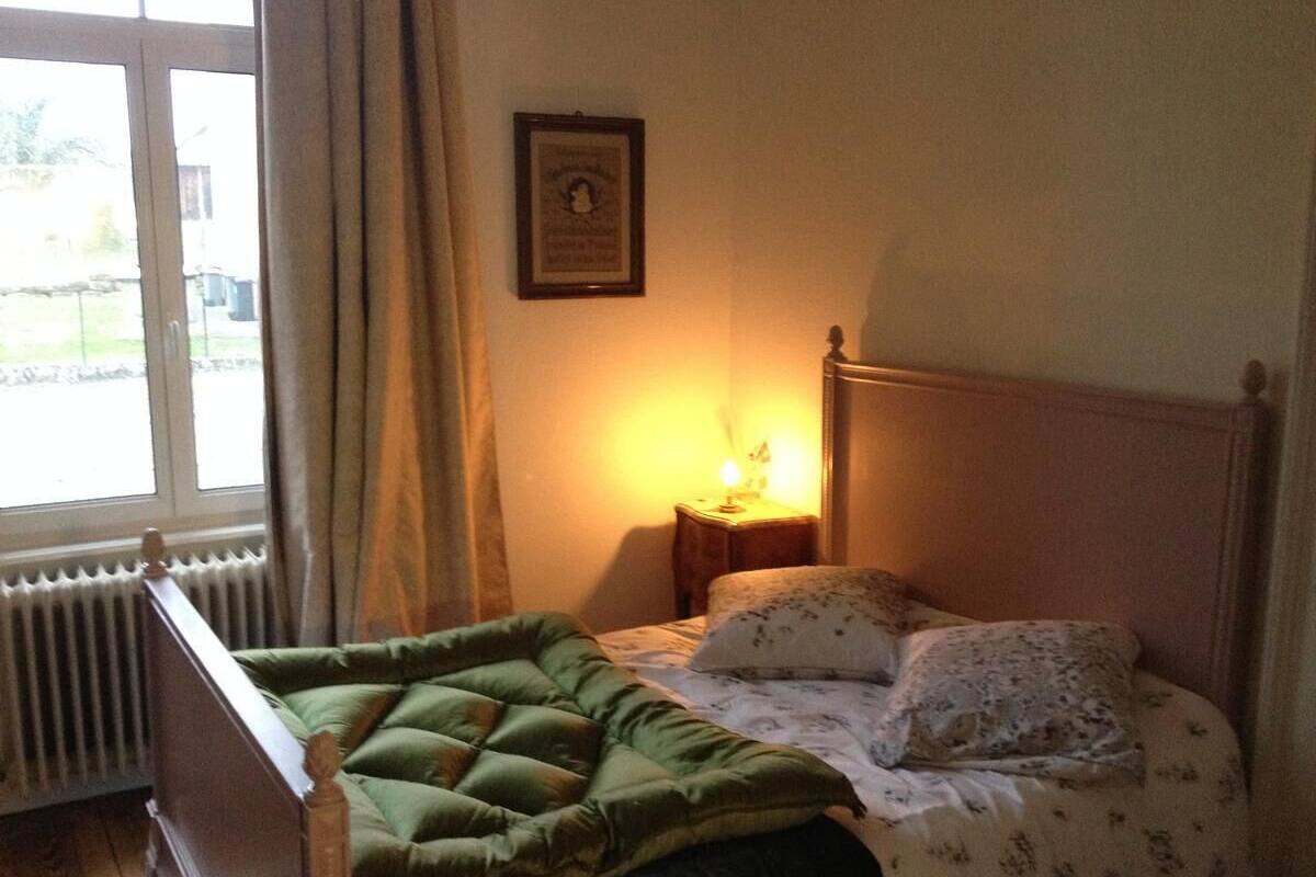 A bedroom with a bed, a nightstand, a framed picture on the wall, and a window with curtains.