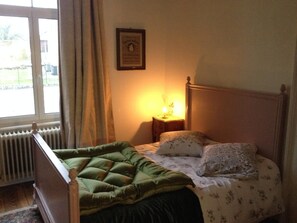 A bedroom with a bed, a nightstand, a framed picture on the wall, and a window with curtains. - L' Obsidienne (Lixheim)