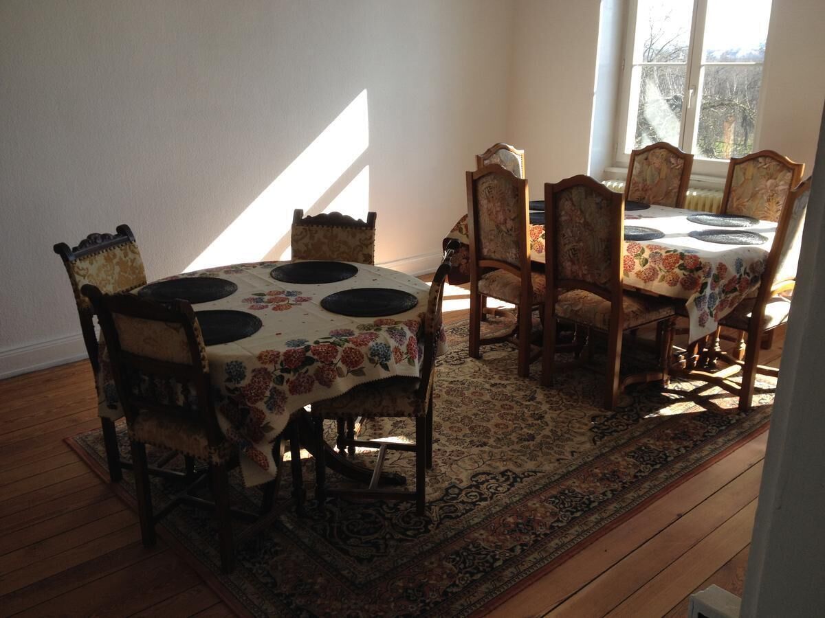 Een eethoek met een tafel en stoelen, een kamerkleed met een patroon en een uitzicht door een raam.