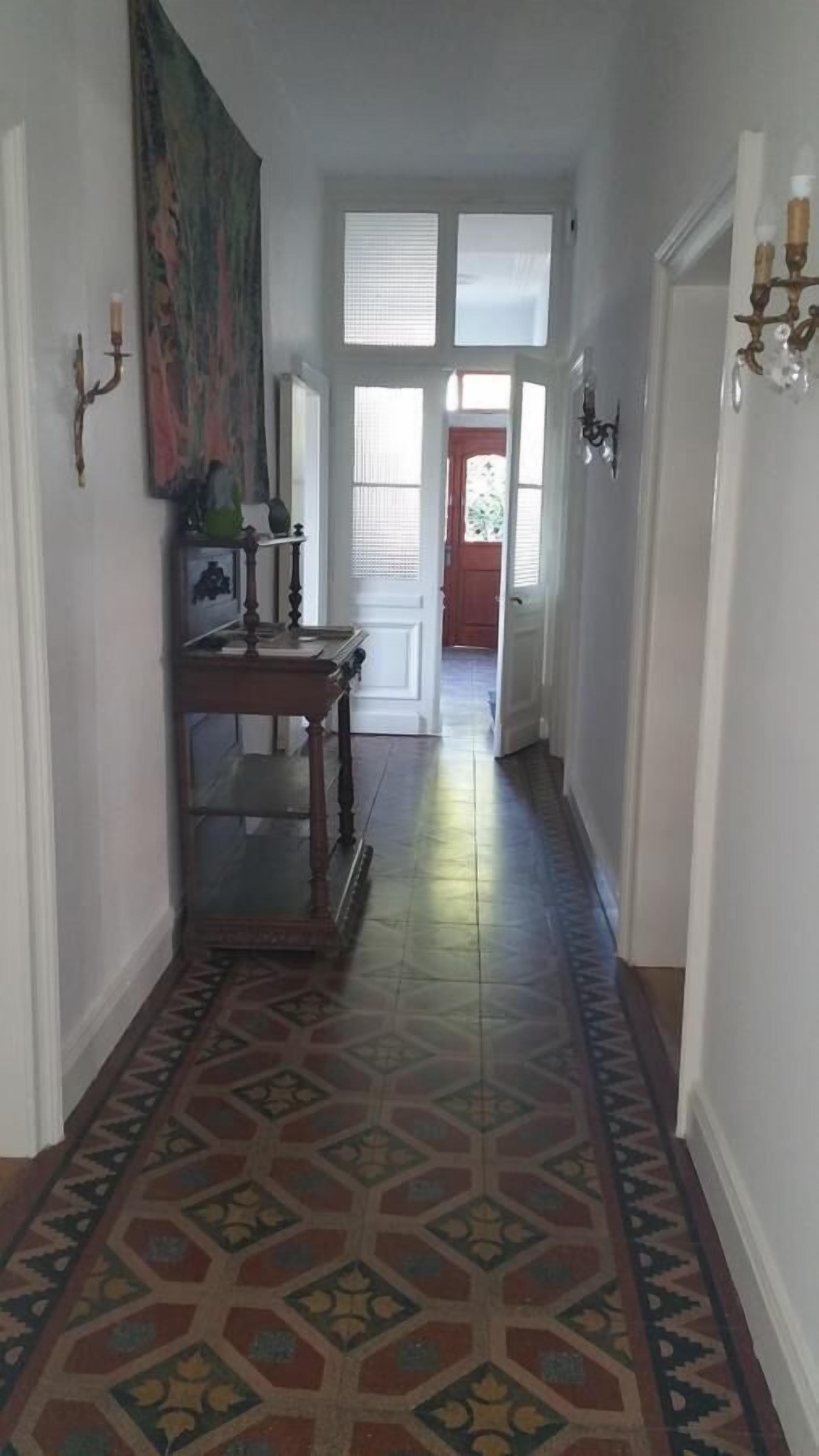 A hallway with patterned floor tiles, a wooden bench, and a painting on the wall.