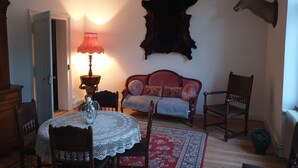 A room with a round table, chairs, a lamp, a sofa, and a mounted animal head. - L' Obsidienne (Lixheim)