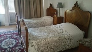 A hotel room with two wooden beds, a red patterned carpet, a wooden nightstand with a lamp, and a window with curtains. - L' Obsidienne (Lixheim)