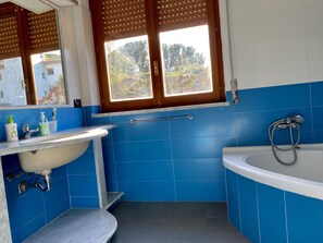 A bathroom with a sink, mirror, window, and bathtub.