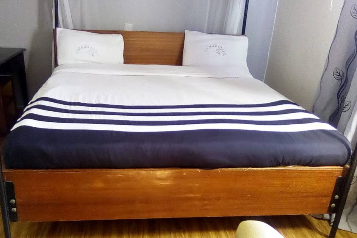 A bed with a wooden frame, white and navy blue striped bedding, and two pillows with a logo.