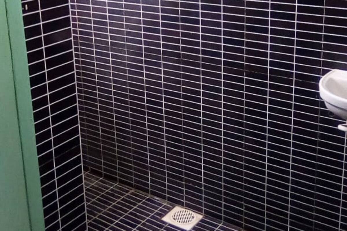 A small, enclosed shower area with black tiled walls and a white toilet visible to the right.