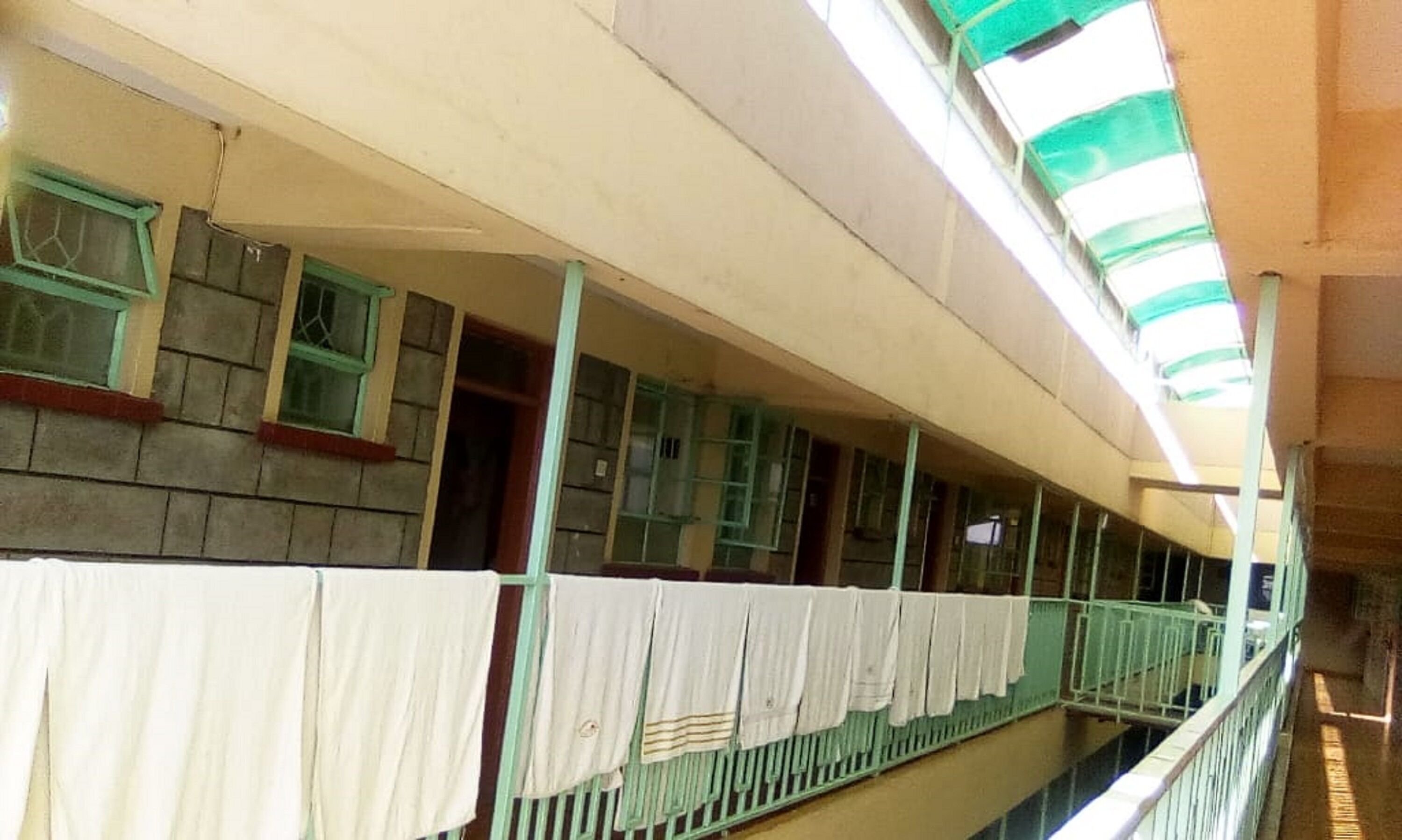 A multi-level corridor with a balcony on the upper floor, featuring a series of windows and a green railing.