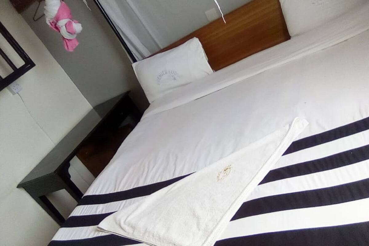 A neatly made bed with white and navy stripes, a wooden headboard, and a white pillow with a logo.