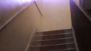 A flight of dark wooden stairs with a handrail on the left, leading to a landing with a light-colored wall. - Scarlet Holiday Inn (Nakuru)