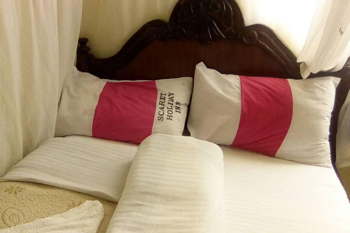 A bed with white and pink pillows, a wooden headboard, and a white curtain.