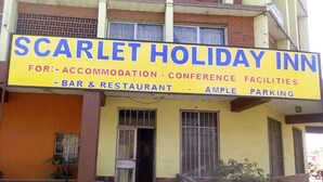 A building with a sign for Scarlet Holiday Inn, offering accommodation, conference facilities, a bar and restaurant, and ample parking. - Scarlet Holiday Inn (Nakuru)