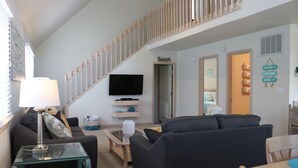 A living room with a staircase, a flat-screen TV mounted on the wall, and a sign reading "Beach". - Bright & Beachy 3 bed/2 bath Soundside MP6 (Kill Devil Hills)