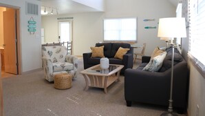A living room with a high ceiling, a glass coffee table, two sofas, a chair, and a lamp. - Bright & Beachy 3 bed/2 bath Soundside MP6 (Kill Devil Hills)