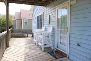 A wooden deck with white chairs and a bench, a sliding glass door, and a welcome mat. - Bright & Beachy 3 bed/2 bath Soundside MP6 (Kill Devil Hills)
