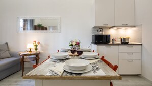 A dining area with a wooden table set for two, a sofa, a small side table with a lamp, and a kitchen area with cabinets and appliances. - Central Station Apartment by Mmega (Florence)