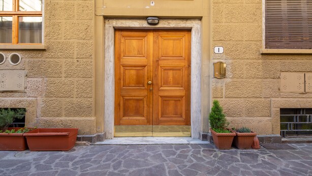 A double wooden door with a brass handle, flanked by two potted plants, set in a stone-paved entrance area. - Central Station Apartment by Mmega (Florence)