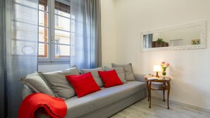 A living room with a grey sofa, red cushions, a small wooden side table with a lamp, and a mirror on the wall. - Central Station Apartment by Mmega (Florence)
