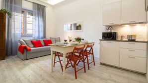 A modern living room with a sofa, dining table, and chairs, a kitchen with cabinets and appliances, and a window with curtains. - Central Station Apartment by Mmega (Florence)