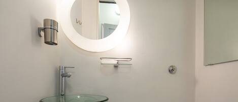 A bathroom with a glass bowl sink, a round mirror with a light, and a wall-mounted towel rack.