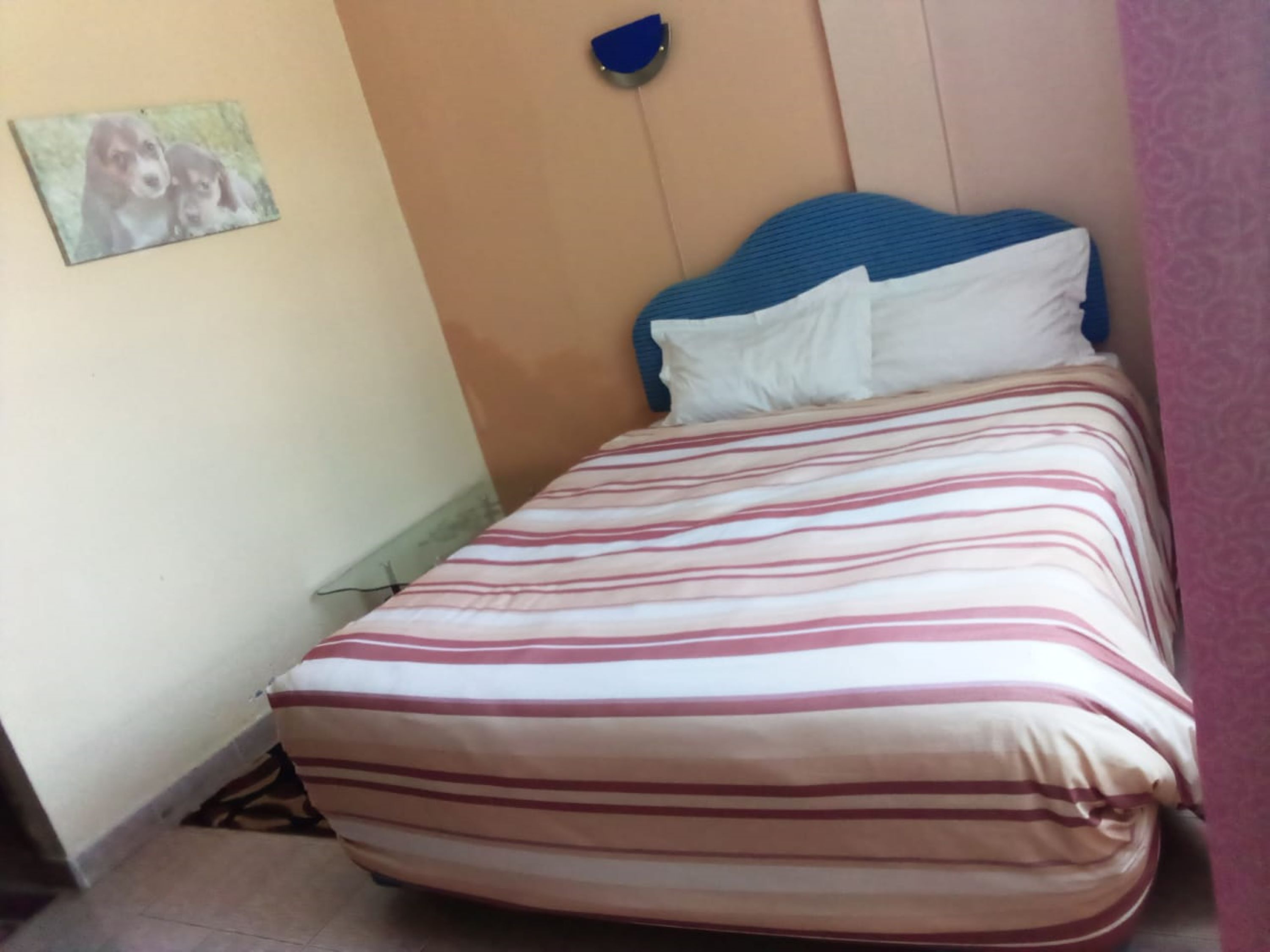 A bed with a striped bedspread, a blue headboard, and a wall-mounted light fixture.