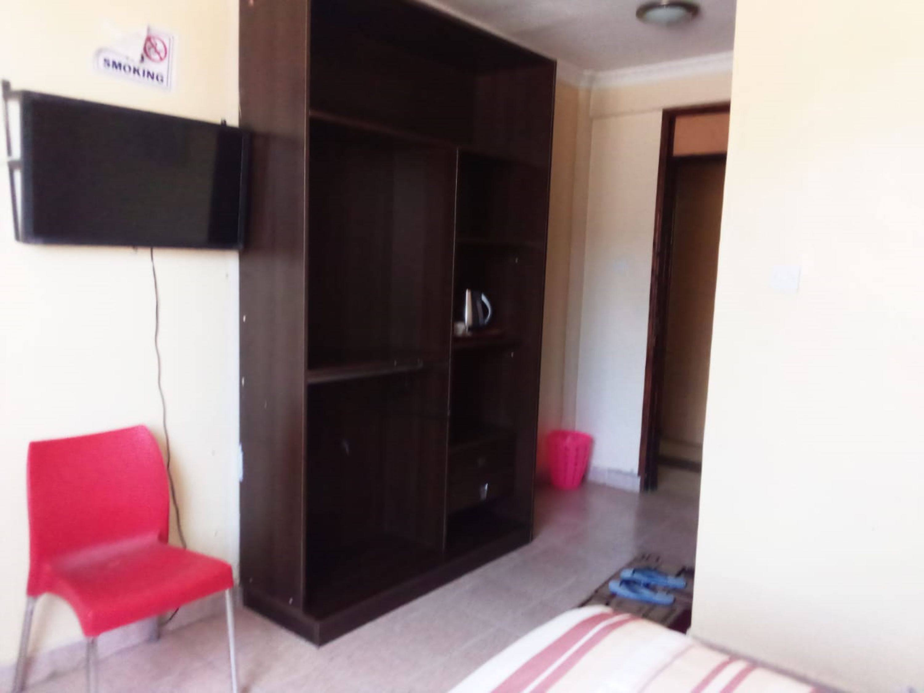 A room with a large wardrobe, a red chair, and a television mounted on the wall.