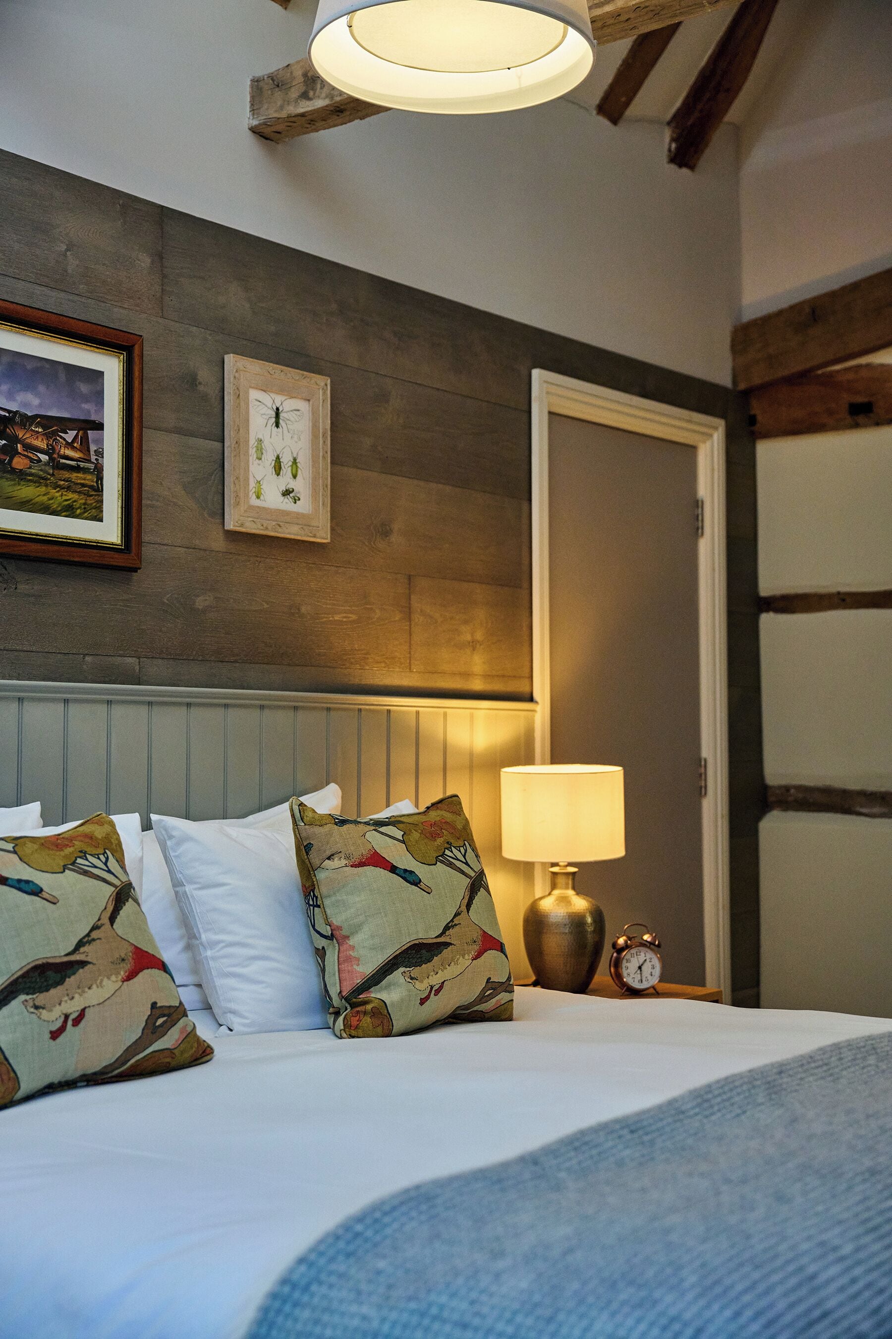 A neatly made bed with patterned pillows, a bedside lamp, and an alarm clock.