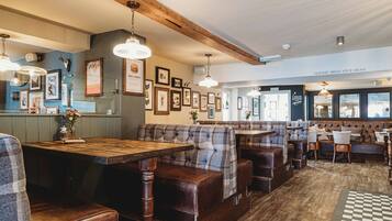 A restaurant with wooden tables and benches, framed pictures on the walls, and a sign for the toilets upstairs.